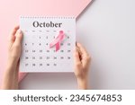 Small photo of Support breast cancer awareness in October. Top view of hands holding a calendar and pink ribbon on separated pastel pink and white backdrop, providing copyspace for text or advertising purposes