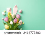 Small photo of Easter happiness in photo! Overhead perspective of a bouquet adorned with tulips and vibrant eggs, complemented by quirky bunny ears. Displayed on mint-green background, ready for personalized message