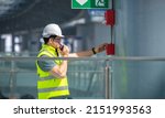 Small photo of Engineer wearing safety uniform and helmet under checking fire evacuation alarm emergency system in industry factory and exit door is factory security protection concept.