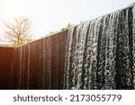 Small photo of The highlight of place is the flowing water like a small waterfall curtain. Water overflowing the mortar weir during the rainy season with tree and sunlight at Pang Sawan Weir, Uthai Thani, Thailand.