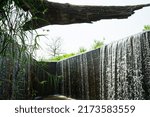 Small photo of Place is the flowing water like a small waterfall curtain. Water overflowing the mortar weir during the rainy season with Log wood and white background at Pang Sawan Weir, Uthai Thani, Thailand.