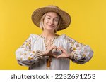 Ukrainian woman showing sign of shape heart. Yellow background. Women health, volunteering, charity donation, help and trust relationships concept.