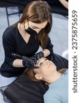 Small photo of Woman professional permanent make-up artist with a permanent make-up tool. A young permanent makeup artist makes permanent eyebrow makeup