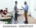 Side view of african american teacher pointing at wristwatch to latecomer schoolboy in classroom