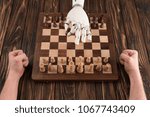 cropped shot of robot playing chess with human on wooden tabletop
