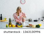 happy young woman preparing tasty nutritious smoothie in blender 
