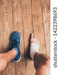 Small photo of partial view of injured sportsman sitting in one sneaker with one foot in elastic bandage