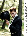 Small photo of handsome aristocratic man holding hat while standing in suit