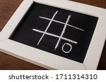 Small photo of tic tac toe game on blackboard with chalk grid and naught on wooden surface