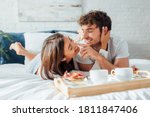 Selective focus of young couple touching each other near coffee and pancakes on breakfast tray on bed