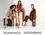 full length of stylish multicultural women in suits sitting on suitcases on white
