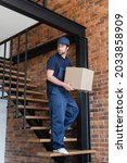 Small photo of mover in overalls holding carton box while walking downstairs