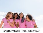 Cheerful multiethnic women with ribbons of breast cancer awareness hugging outdoors