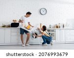 Small photo of happy african american woman looking at boyfriend holding basket with dirty laundry near washing machine in kitchen