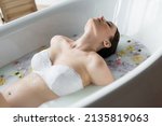 Pregnant woman in lace bra relaxing in milk bath with flowers