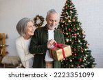 smiling woman hugging mature bearded husband with christmas present