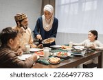 African american woman in hijab serving food on plate near family and ramadan dinner