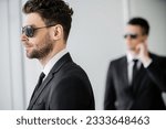 Small photo of surveillance, bodyguard in sunglasses and black suit with tie, hotel safety, security management, uniformed guard on duty, work partner on blurred background, personal protection