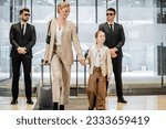 Small photo of personal security service, two bodyguards in formal wear and sunglasses standing near hotel entrance, happy mother and child holding hands and walking with luggage, entering lobby, luxury lifestyle