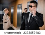 Small photo of bodyguard service, personal protection, blonde woman in formal wear standing near elevators, security personnel protecting successful businesswoman in hotel, handsome man with earpiece