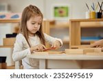 Small photo of girl playing with wooden didactic materials near friend in class in montessori school