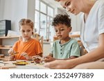 Small photo of interracial children playing with didactic montessori material near female teacher, diversity