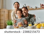 Small photo of joyous african american family hugging warmly and smiling joyfully at camera at breakfast table