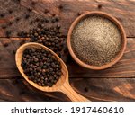 Black peppercorns in a spoon and black ground pepper in a plate close-up on a wooden background. Top view