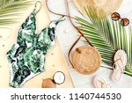 Woman's beach accessories: swimsuit with tropical print, rattan bag, straw hat, tropical palm leaves on yellow background. Summer background. Flat lay, top view.
