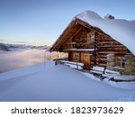 Snow covered mountain hut old farmhouse in the ski region of Saalbach Hinterglemm in the Austrian alps at sunrise against blue sky
