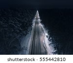 Night time aerial view of a snowy road surrounded pine tree forest in winter season.