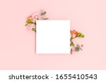 Blank paper card mockup with frame made of flowers and eucalyptus. Festive floral composition with copy space on a pink pastel background.
