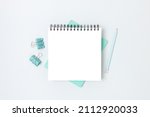 Minimal workspace with square notepad mockup and stationery on a blue background. Monochrome school concept with copyspace.