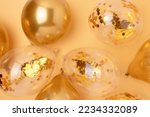 Inflatable balloons with confetti inside on a gold colored background. Festive creative concept. Selective focus.