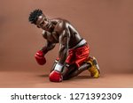 Small photo of Muscular African American Black male sweaty boxer on knees, knocked down trying to get up with dramatic lighting with a brown background
