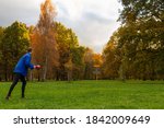 Young caucasian man in blue jacket playing disc golf on autumn play course with basket