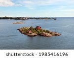 Aerial view on little islands with tiny red houses in Scandinavian style among the vast water ocean or sea, under blue sky. Outdoors, copy space.