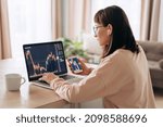 Small photo of Young business woman trader analyst looking at laptop monitor, holding smartphone. Investor broker analyzing indexes, trading online investment data on cryptocurrency stock market graph at home