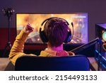 Back view of professional gamer sitting in gaming chair and celebrating his victory in online esport tournament, makes winner hand gesture, wearing headset, looking on monitor. Neon light. Cyber sport