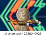 Image of bitcoins lying on mirror surface with one one standing isolated on blurred background with red and green candlesticks on digital crypto chart