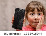 Portrait of a scared little girl with a broken mobile phone. A sad child broke the screen of a mobile phone. Cracked display in hand kids. The frightened child accidentally ruined the smartphone