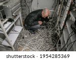 Small photo of The man is in a plundered server room. A sad technician sits near a pile of wires and holds his head with his hands in an empty datacenter.