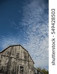 Small photo of Abstract traditional Ontario gambrel roof barn, that was black and is weathered and the boards lit up by sunshine. Sky is a deep blue with interesting cloud scapes of cirrus clouds as a background.