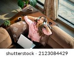 Small photo of A young modern attractive and beautiful Asian Indian Latina female or woman is taking a break from work and absorbed in listening to music with eyes closed in an apartment or interior house setup.