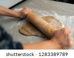 Two hands rolling, the biscuit dough evenly over flour with a rolling pin, making cookies and gingerbread in the kitchen for christmas