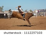 A cowboy competing in a bullriding event at a country rodeo