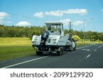 Small photo of Bruce Highway, Proserpine, Queensland, Australia - December 2021: A motor boat on trailer towed by small truck parked on side of a country road