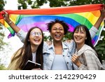 Diversity young gay women with Asian gay waving pride rainbow flag in their backs supporting LGBTQ pride in the park. Independence and polygamy. Supporters of the LGBT community
