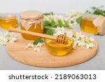 Small photo of Sweet honey jar surrounded spring acacia blossoms. Honey flows from a spoon in a jar. jars of clear fresh acacia honey on wooden background.