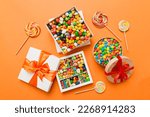 Set of different sweet candy in a paper box with a satin ribbon on a colored background. Holiday concept.
